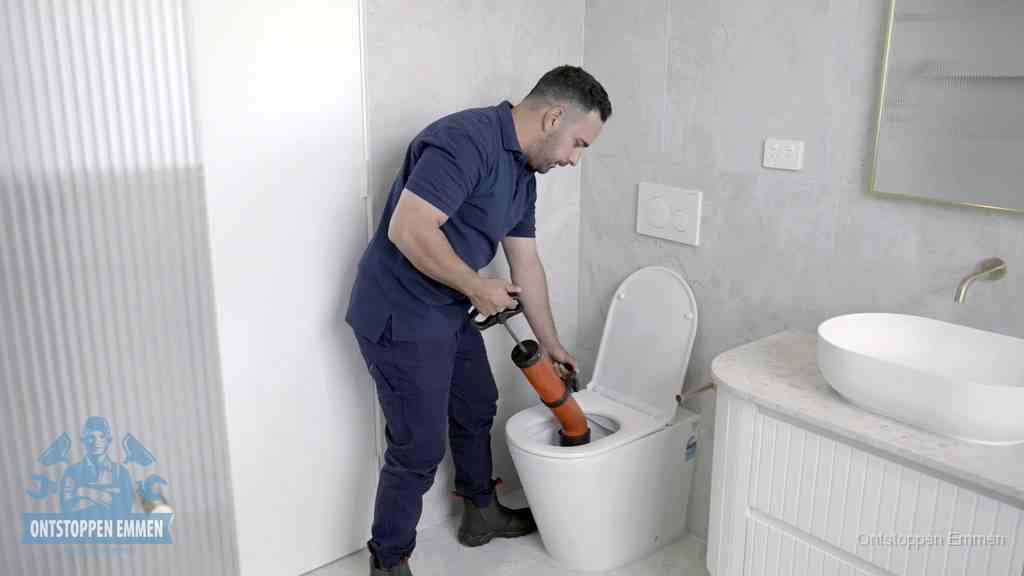 Een monteur buigt over een wandcloset en duwt met de hand een persluchtontstopper in de toiletpot om de verstopping handmatig los te maken in Emmen