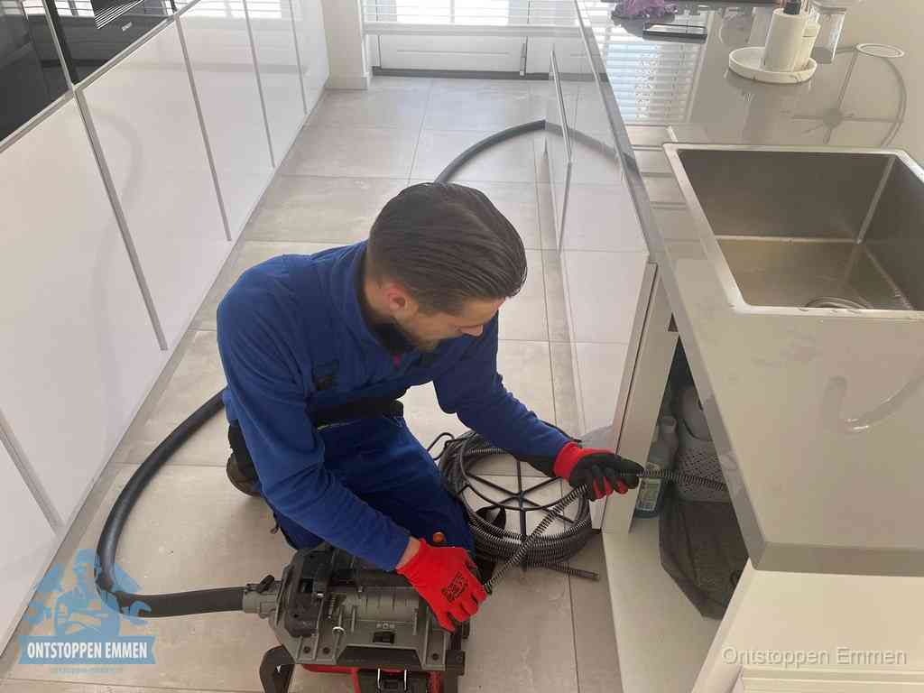 Een monteur ontstopt de keukenafvoer onder de spoelbak met een elektrische veermachine in Emmen