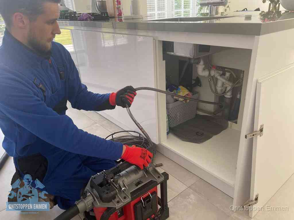Monteur voert een ontstoppingsveer in de afvoer onder de keuken in Emmen