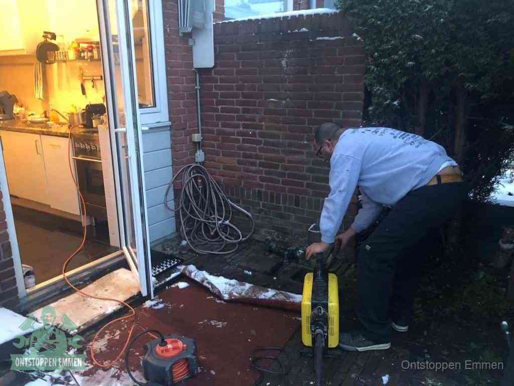 Een monteur werkt buiten bij een open riool-/grondput met een elektrische ontstoppingsmachine om een verborgen afvoerprobleem op te sporen in Emmen