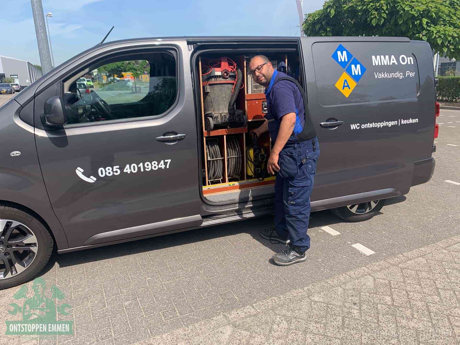Een monteur bij de open schuifdeur van zijn bedrijfsbus op een parkeerplaats, klaar om de oorzaak van terugkerende afvoerverstoppingen aan te pakken in Emmen