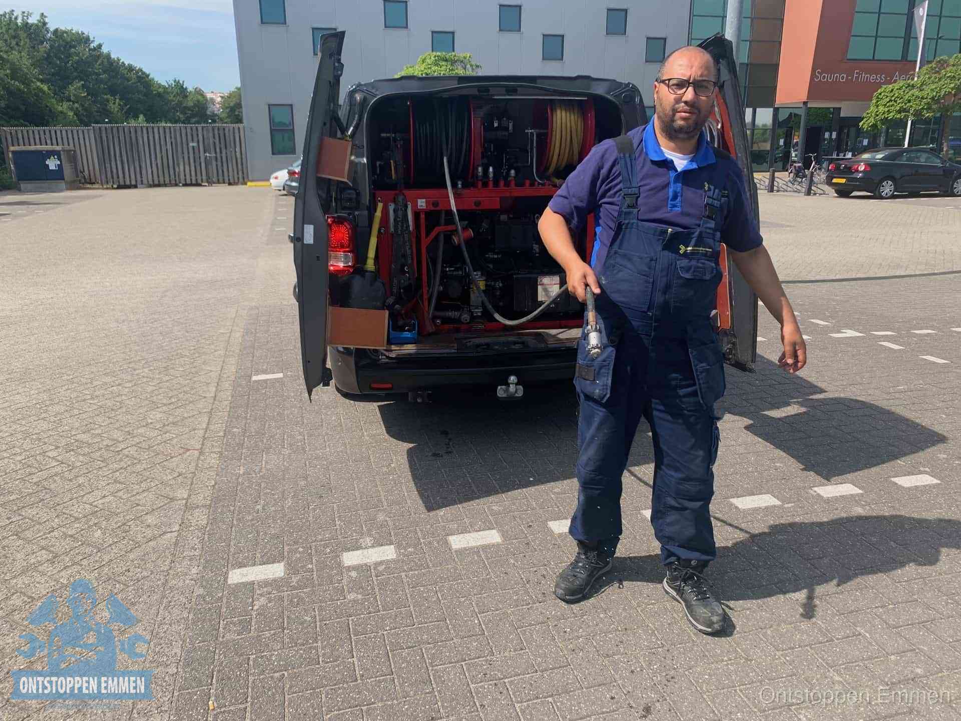 Een monteur bij zijn bestelbus met een hogedruk- en rioolreinigingsunit, klaar om de oorzaak van terugkerende wc-verstoppingen aan te pakken in Emmen