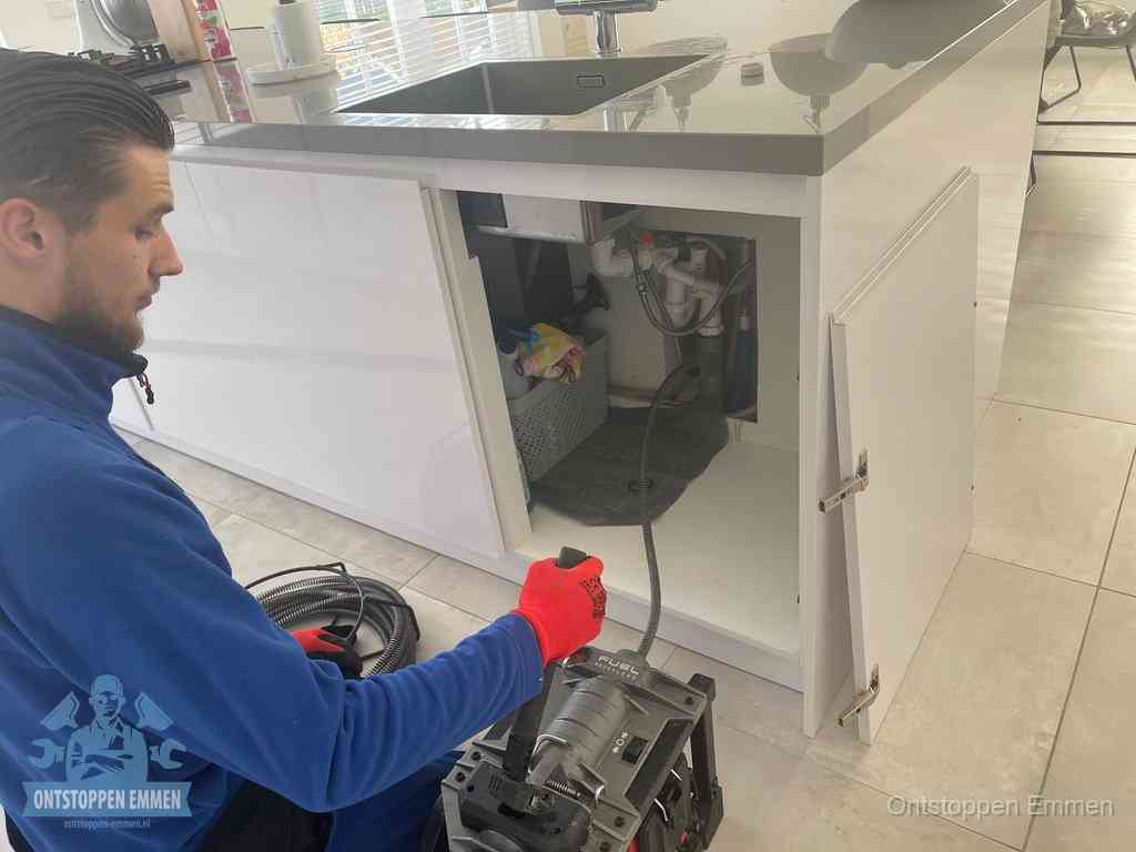 Monteur ontstopt met een veermachine een verstopte afvoer onder de gootsteen in Emmen