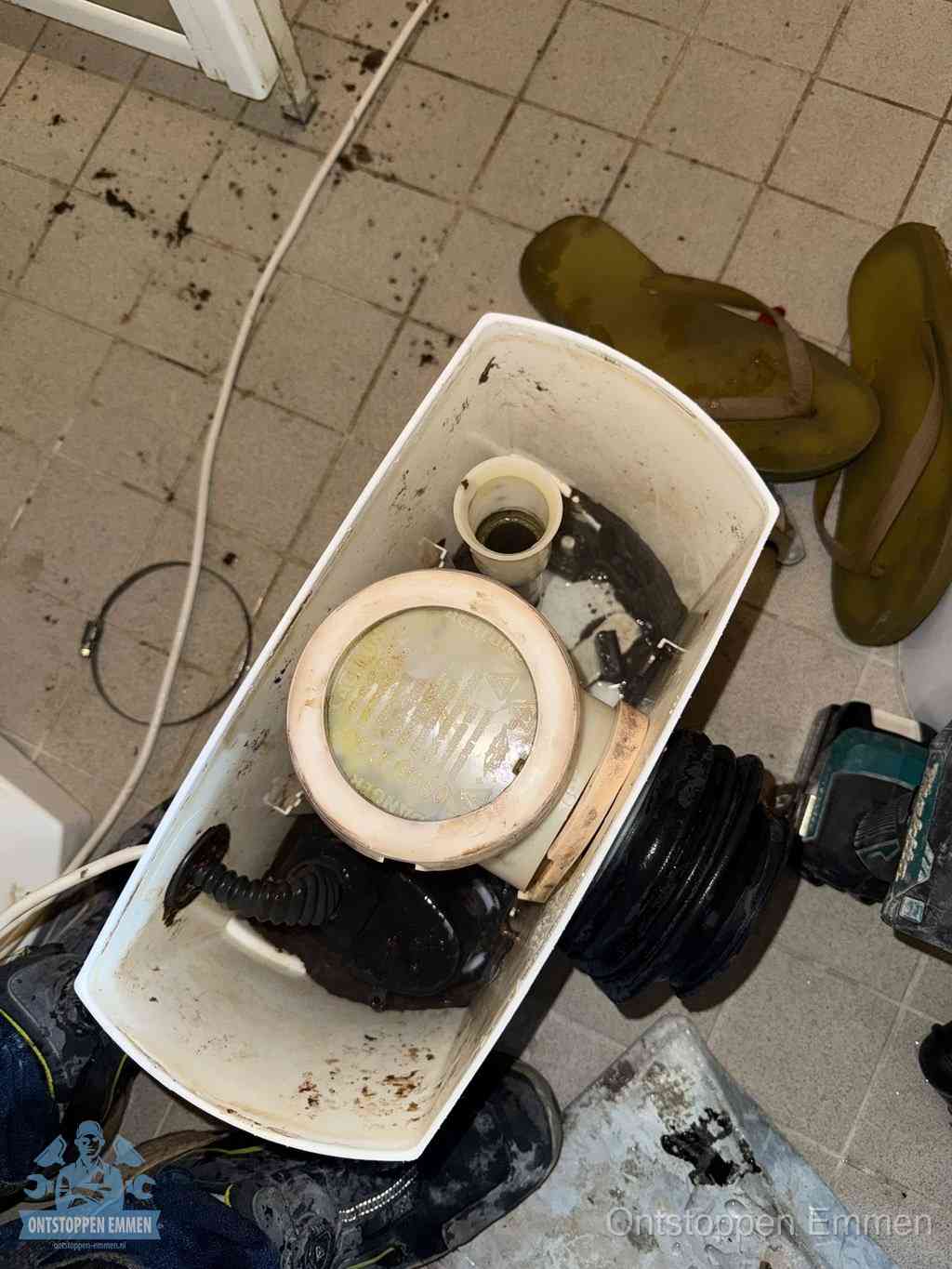 Een gedemonteerde toiletpot op de vloer met ontstoppingsveer en gereedschap ernaast, het verwijderen van een vastzittend voorwerp uit de wc in Emmen