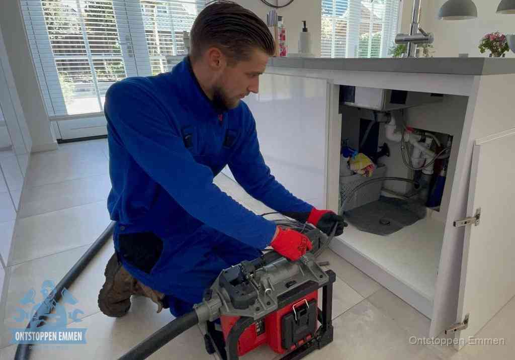 Een monteur voert een professionele elektrische ontstoppingsmachine in de afvoer onder de spoelbak tijdens het gootsteen ontstoppen in Emmen