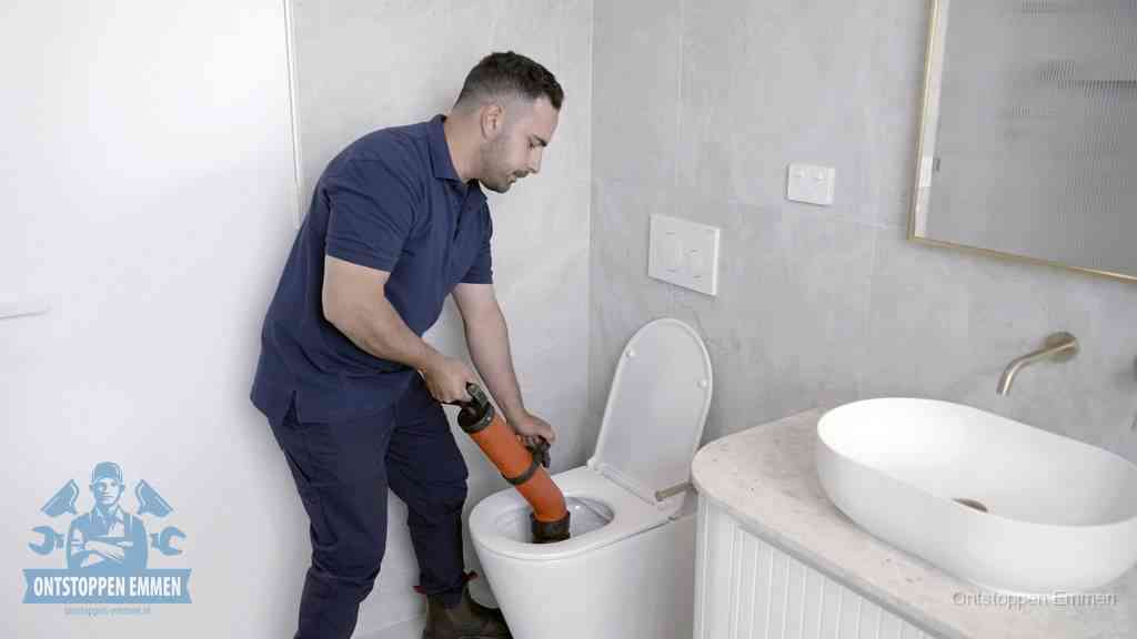 Een man gebruikt een handmatige luchtdruk-ontstopper in een modern betegeld toilet om zelf de wc te ontstoppen in Emmen